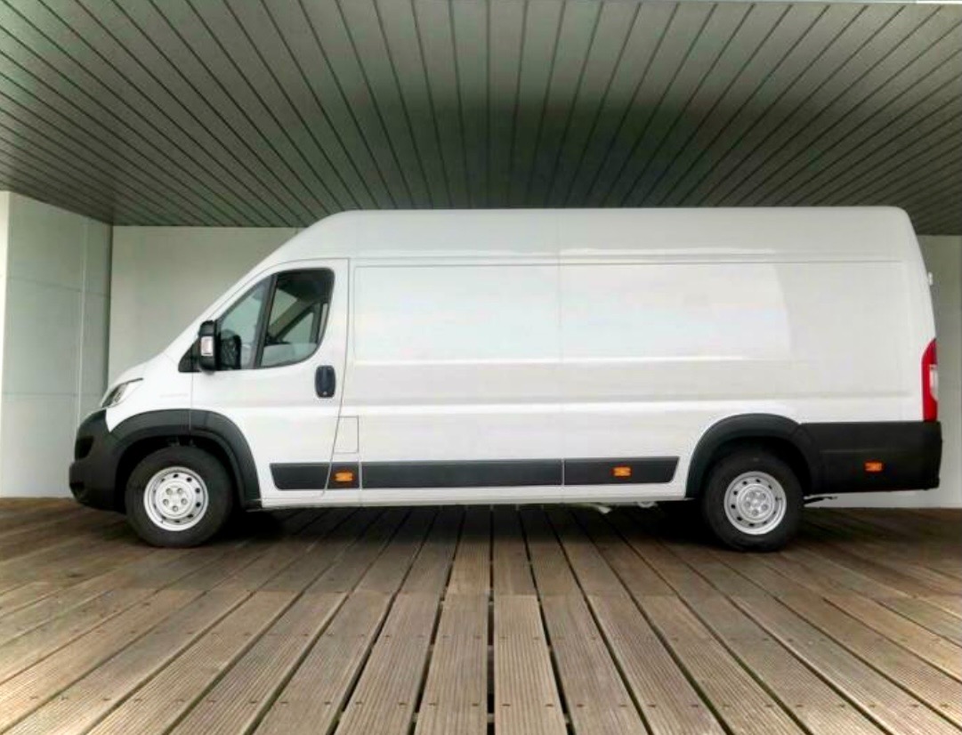 Biały, dostawczy bus na drewnianej podłodze w Ijmunden, zaparkowany wewnątrz budynku z metalowym sufitem.