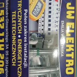 Reklama firmy elektrycznej z bliska: schemat instalacji elektrycznej, multimetr wskazujący 182.2 V, fragment instalacji hydraulicznej w tle i dane kontaktowe firmy.