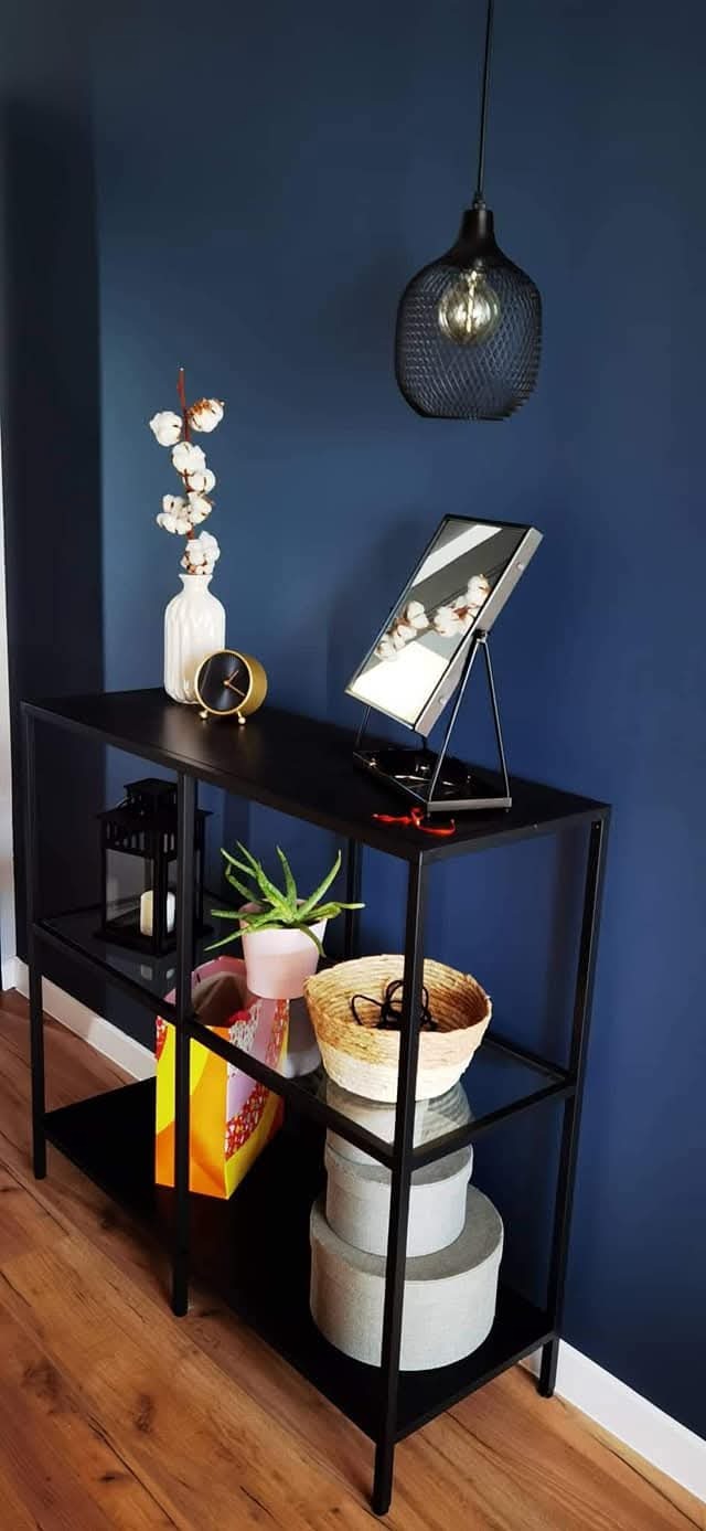Stylowa konsola w loftowym stylu z dekoracjami: wazon z bawełną, zegar, lampa. Granatowa ściana w tle. Aranżacja wnętrza domu deweloperskiego.