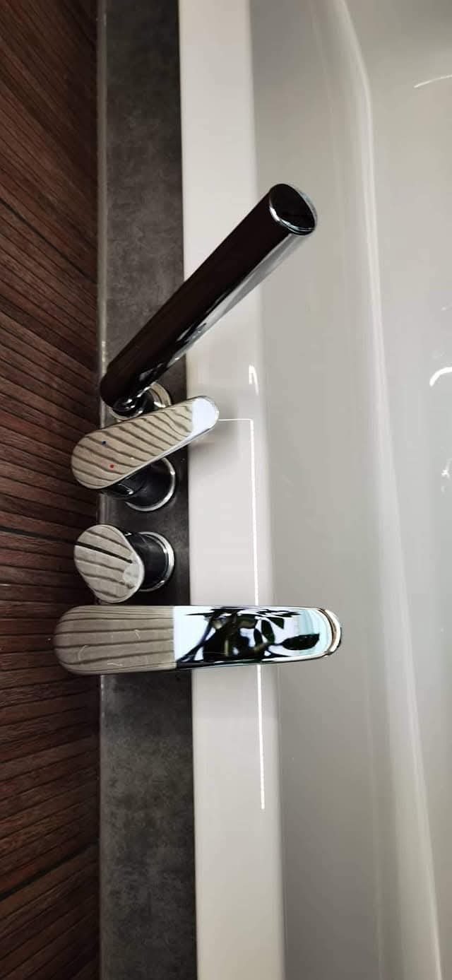 Bateria wannowa z chromowanymi elementami i drewnopodobną okładziną ścienną, zamontowana przy białej wannie. Detal wykończenia łazienki.