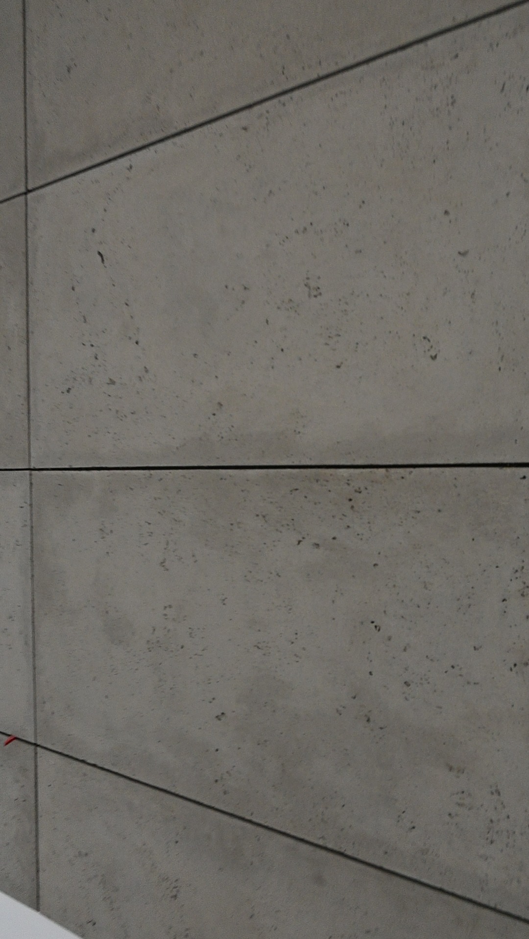 Szare, prostokątne płytki imitujące beton, ułożone poziomo z cienkimi fugami. Widoczna faktura materiału i delikatne cieniowanie. Minimalistyczny design.