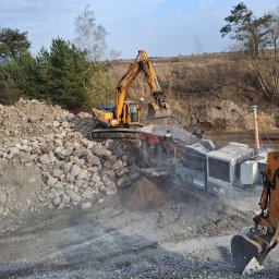 Trans-Kop Bartłomiej Kamiński - Żółta koparka Hyundai ładuje kamienie do kruszarki Sandvik na placu budowy, w tle drzewa i niebo