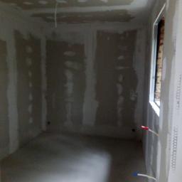 Santa-Bud Krzysztof Biegan - Pokój w trakcie remontu: ściany i sufit pokryte płytami gipsowo-kartonowymi, widoczne szpachlowane łączenia, wystające przewody elektryczne, okno w trakcie montażu.