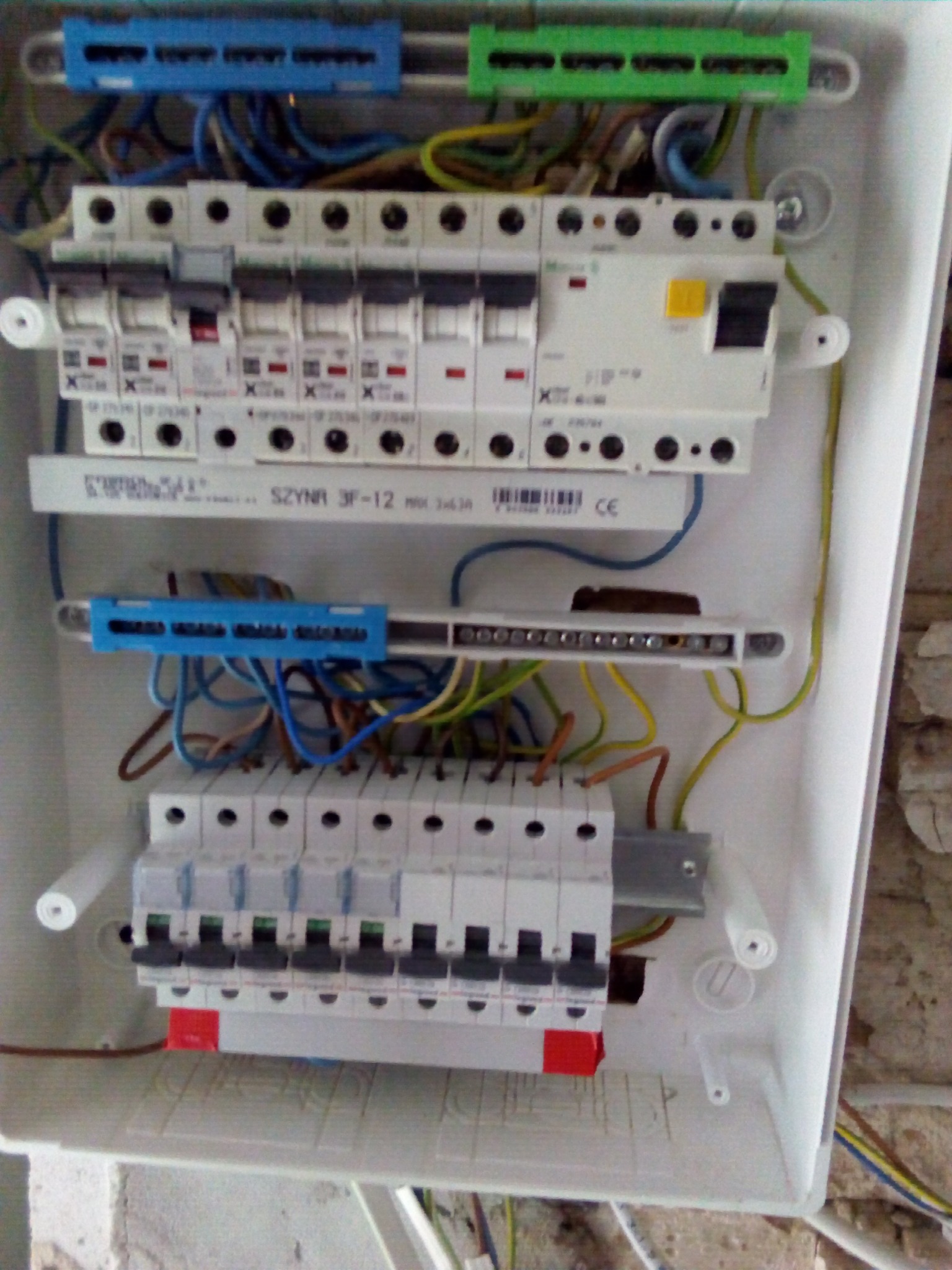 Rozdzielnia elektryczna w trakcie montażu, widoczne przewody, bezpieczniki i szyny montażowe w białej obudowie z tworzywa sztucznego.