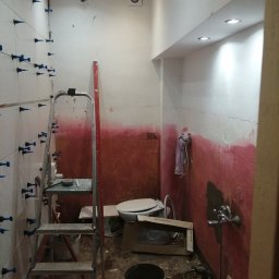 Magdalena Stępień - Łazienka w trakcie remontu: częściowo położone białe płytki z niebieskimi krzyżykami dystansowymi, ściany pomalowane do połowy na czerwono, widoczna drabina, toaleta i narzędzia.