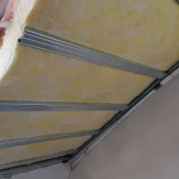 Ocieplenie poddasza wełną mineralną w Przeworsku, widoczne metalowe profile konstrukcyjne i fragment okna dachowego.