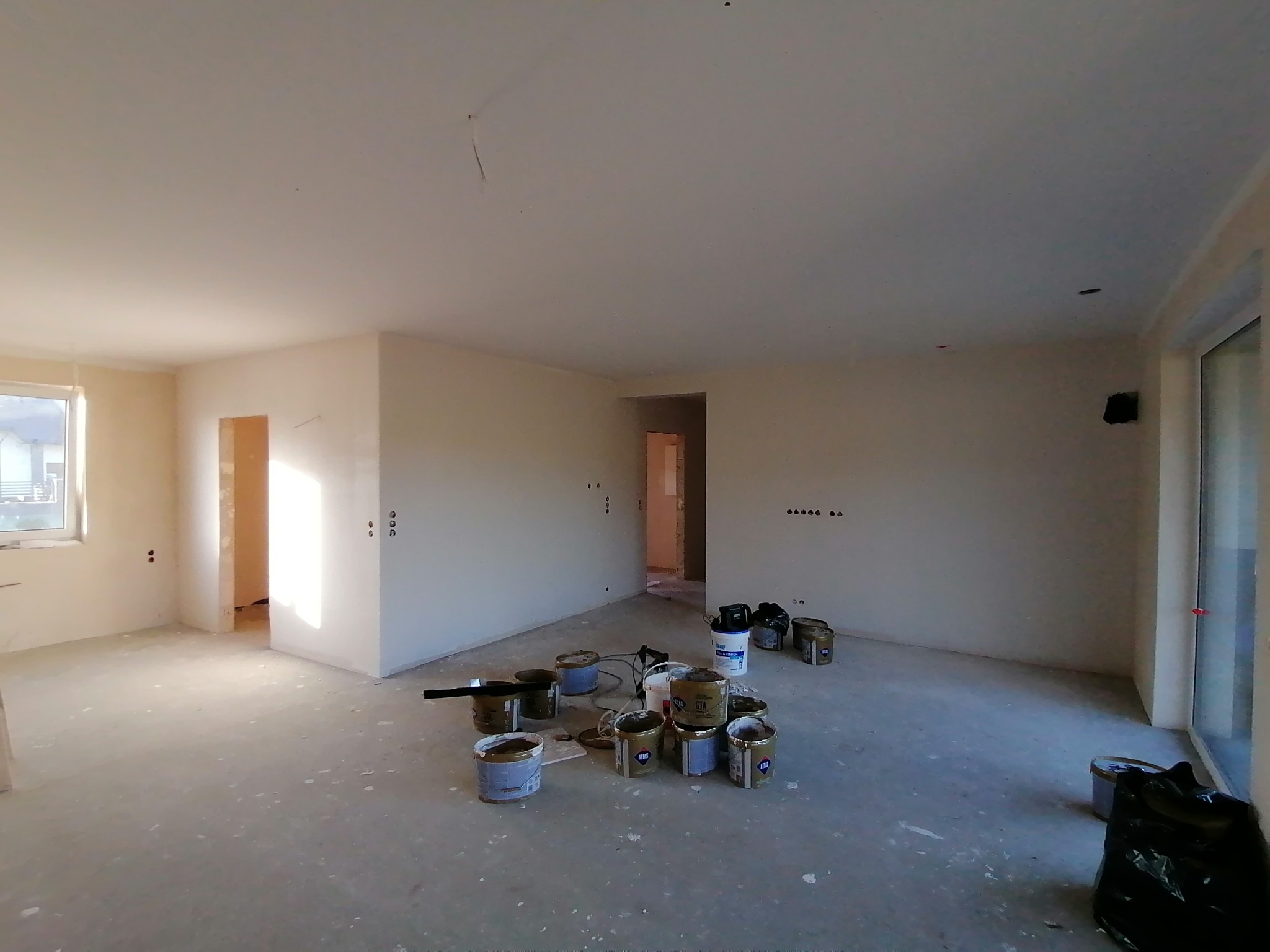 Wnętrze w stanie deweloperskim, przygotowane do malowania ścian, widoczne puszki z farbą Atlas i GTA na podłodze, ściany zagruntowane, widoczne instalacje elektryczne