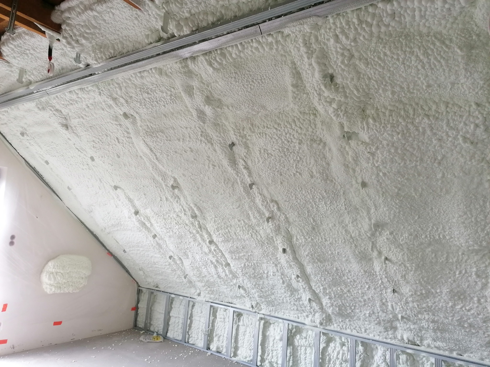 Poddasze ocieplone białą pianką PUR, widoczne metalowe profile konstrukcyjne, fragment ściany z niedokończonym ociepleniem.