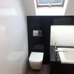 Nowoczesna łazienka na poddaszu z biało-czarnymi płytkami, podwieszaną toaletą i oknem dachowym.