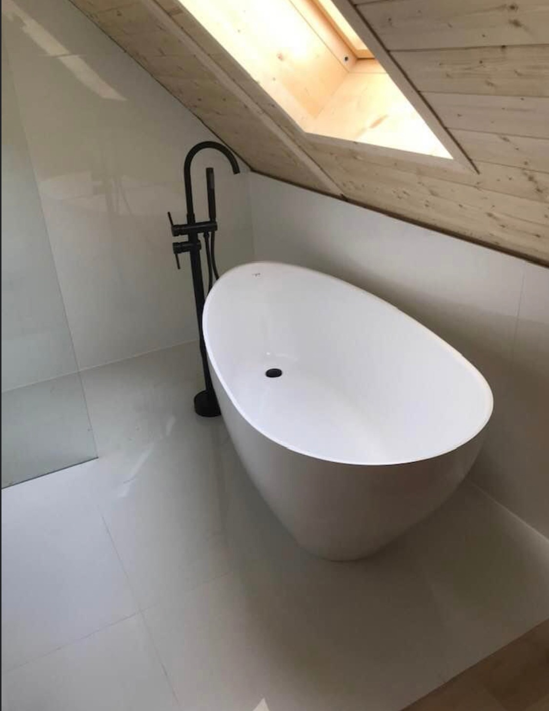 Nowoczesna, wolnostojąca wanna w jasnej łazience na poddaszu w Krakowie, z czarną armaturą i oknem dachowym.