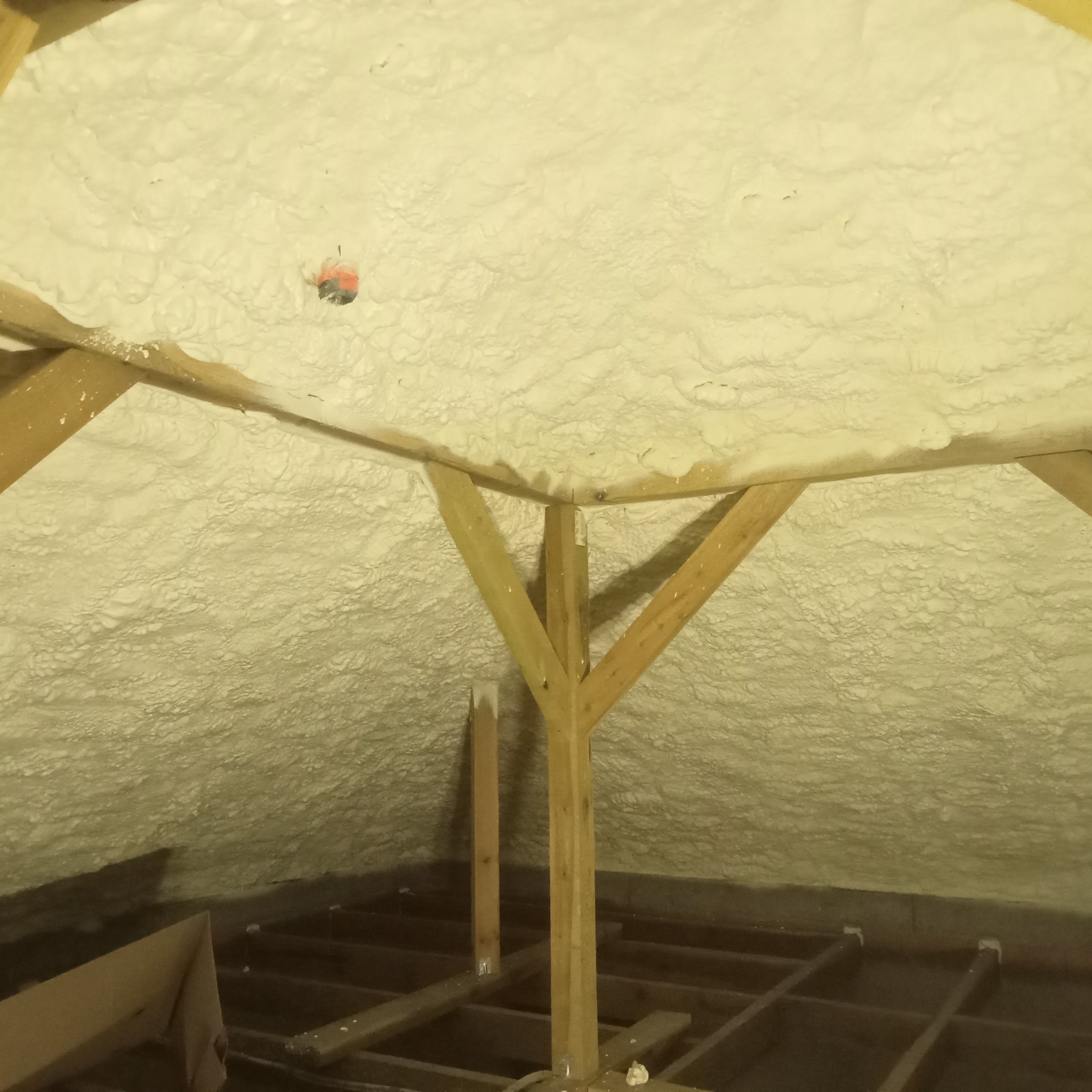 Poddasze po natrysku pianki PUR, widoczne drewniane elementy konstrukcyjne i równomierna warstwa izolacji. Mały element instalacji elektrycznej wystaje z piany.