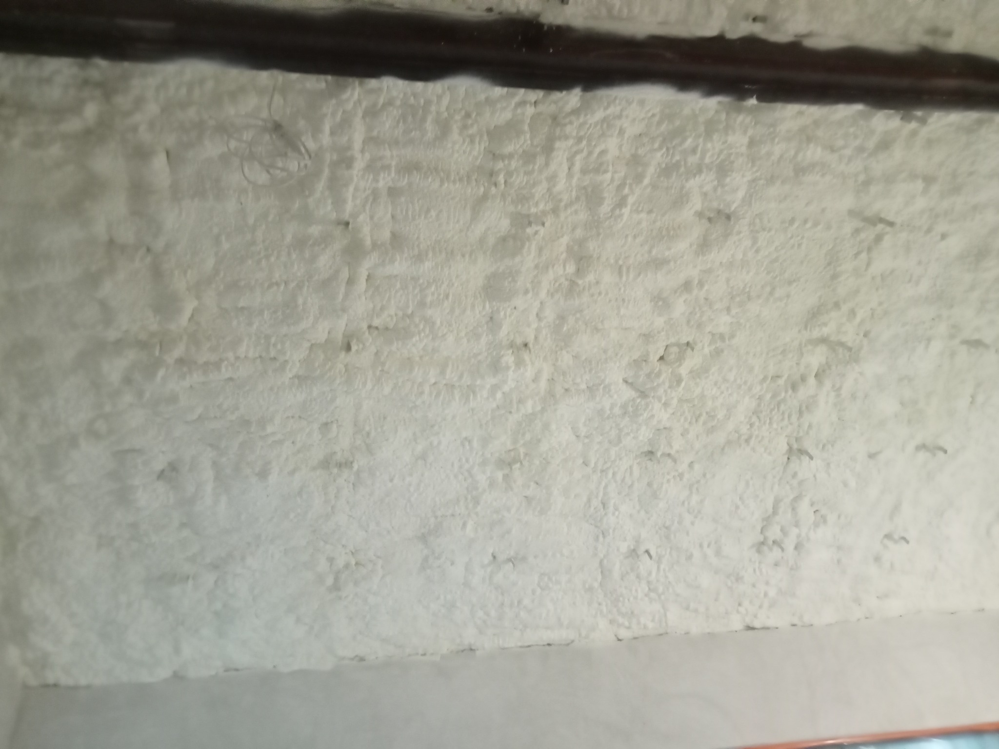 Ściana poddasza po natrysku izolacji. Widoczna struktura pianki, równomierne pokrycie powierzchni. Izolacja termiczna poddasza, detale wykończenia.