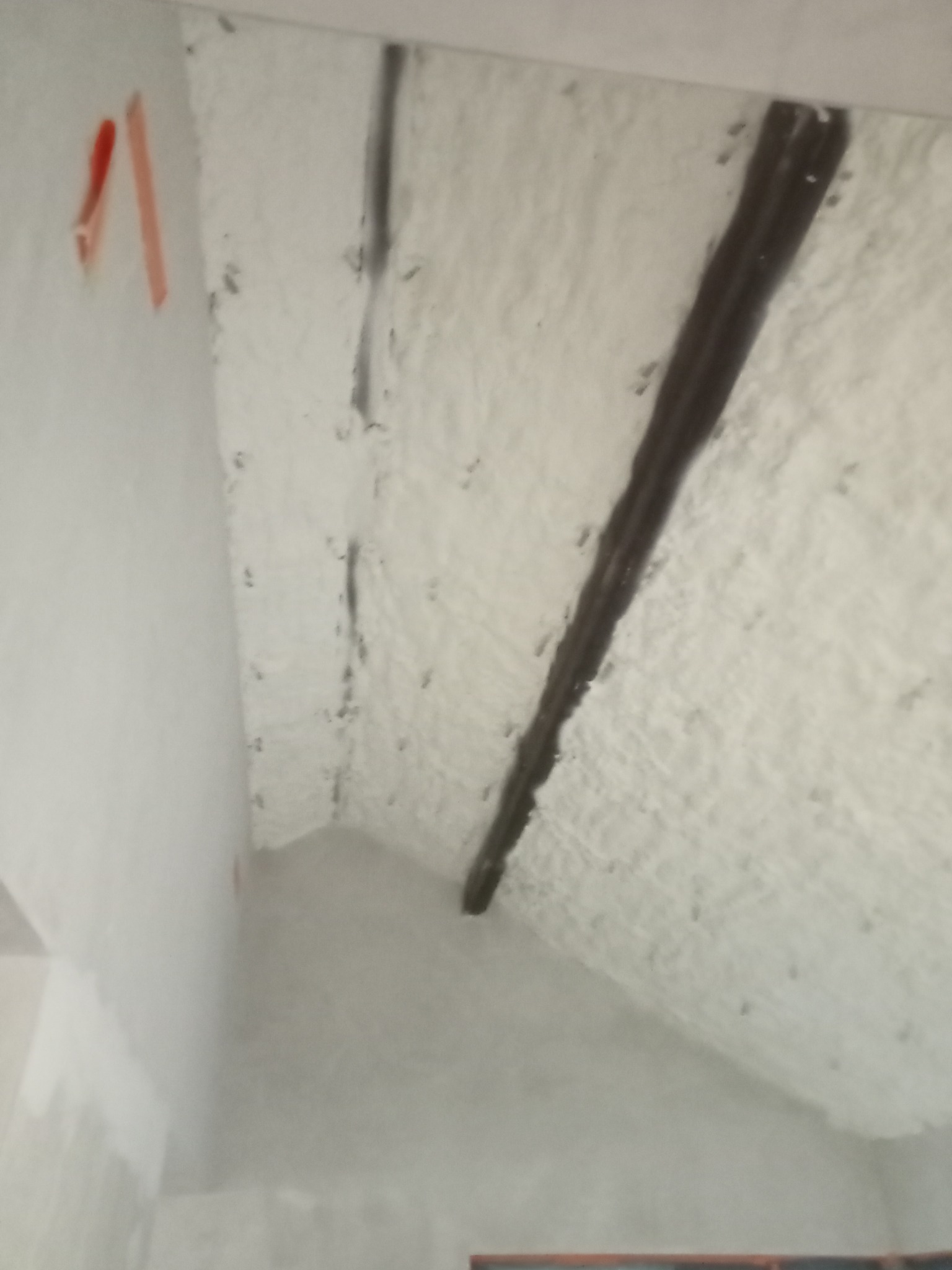 Poddasze po natrysku izolacji piankowej, widoczne elementy konstrukcyjne. Biała, gruba warstwa piany pokrywa skośne powierzchnie. Fragment ściany z taśmą malarską.