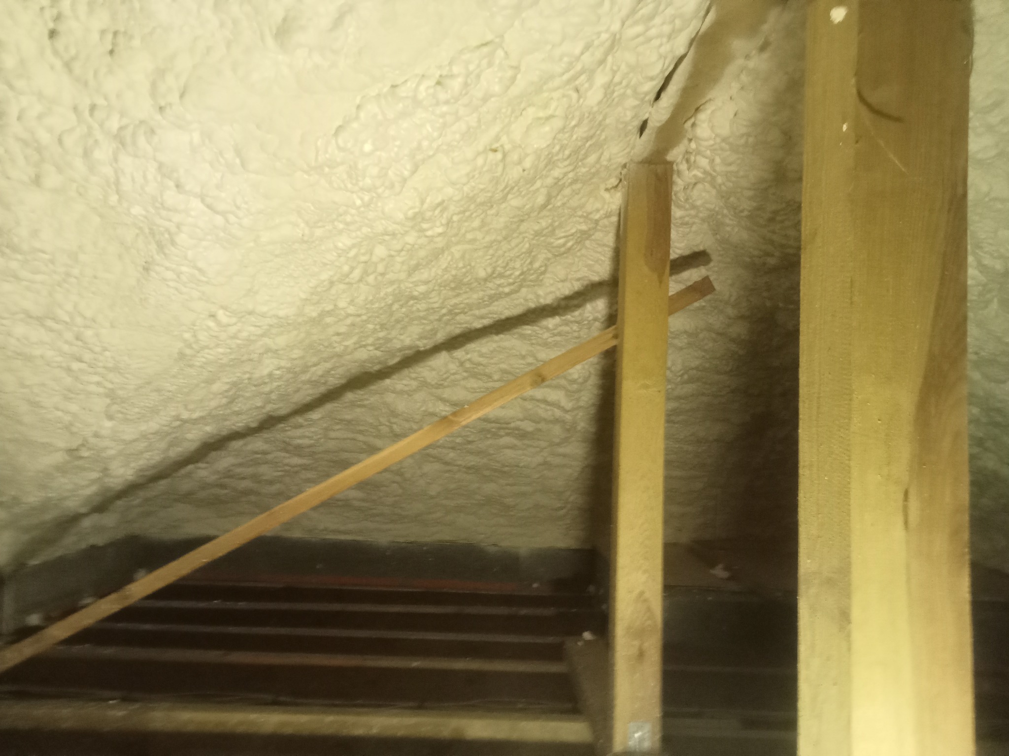 Ocieplenie poddasza pianką, widoczne drewniane elementy konstrukcyjne. Aplikacja pianki w trudno dostępnym miejscu, wypełniająca przestrzeń.