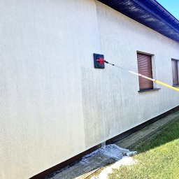 ProClean Grzegorz Rogala - Elewacja budynku jednorodzinnego czyszczona myjką z długim, żółtym teleskopowym uchwytem, woda spływa po ścianie na chodnik.