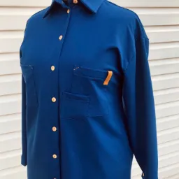 Granatowa sukienka koszulowa z długim rękawem i dwoma kieszeniami na piersiach, zapinana na drewniane guziki, prezentowana na manekinie na tle białej ściany.