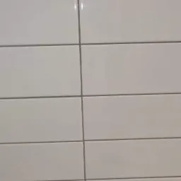 Świeżo umyte, białe, prostokątne płytki ceramiczne ułożone poziomo, z szarymi fugami, widoczne delikatne refleksy światła.