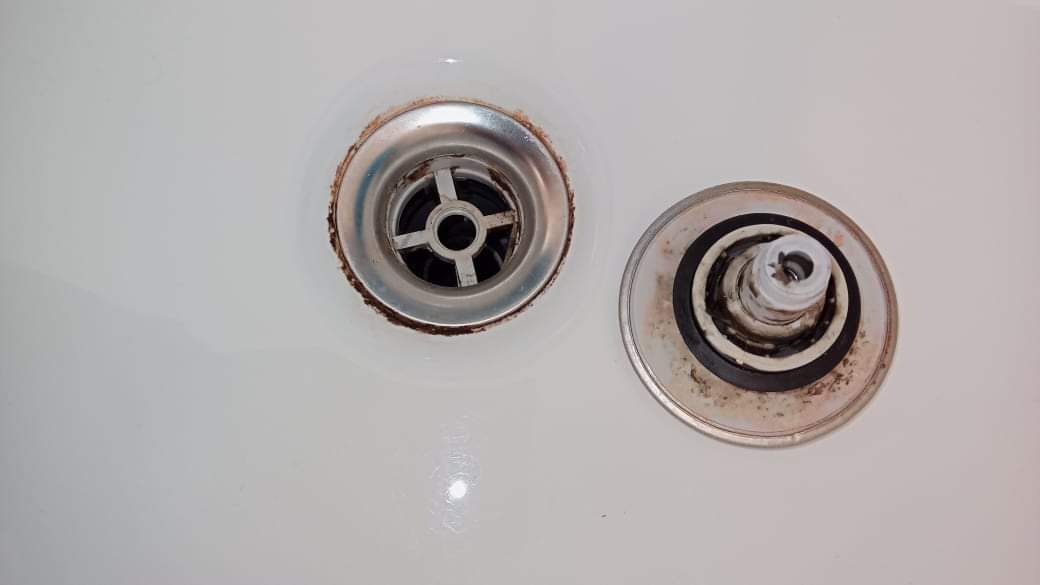Odpływ w wannie z widocznymi śladami rdzy i osadu, obok wyjęty element odpływu z uszczelką.