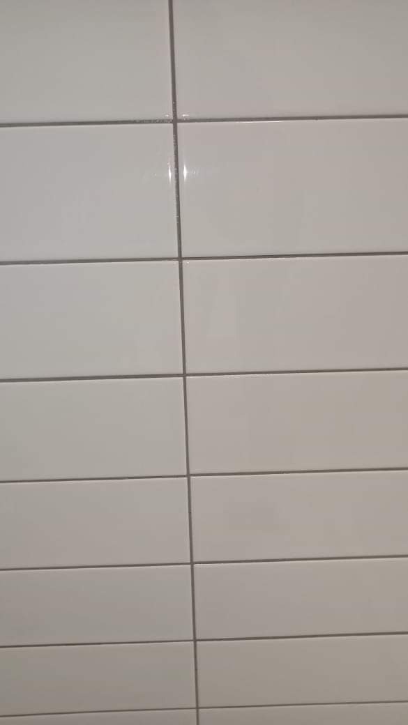 Świeżo umyte, białe, prostokątne płytki ceramiczne ułożone poziomo, z szarymi fugami, widoczne delikatne refleksy światła.