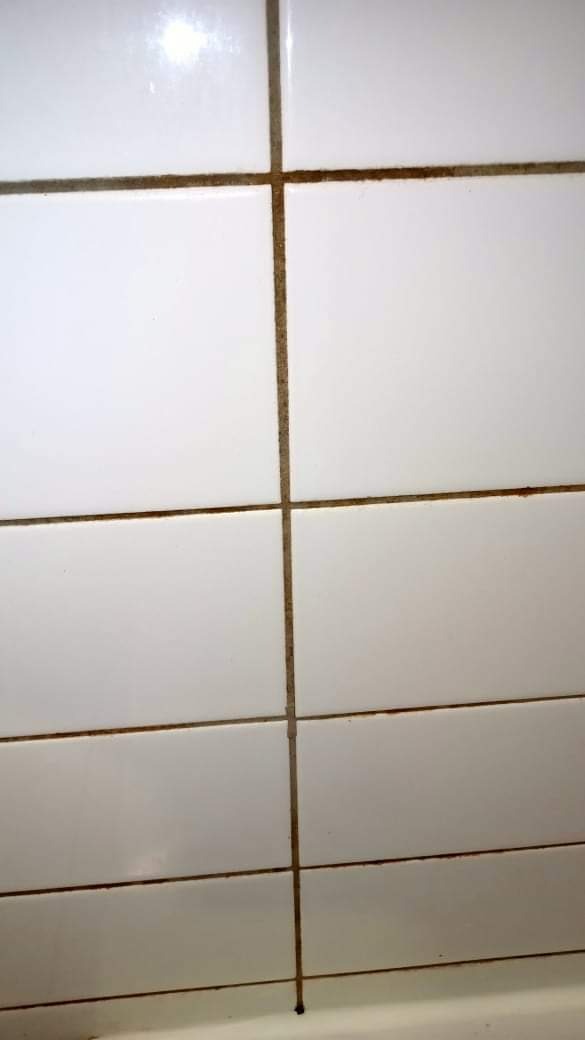 Białe kafelki łazienkowe z widocznym brudem i pleśnią w fugach.