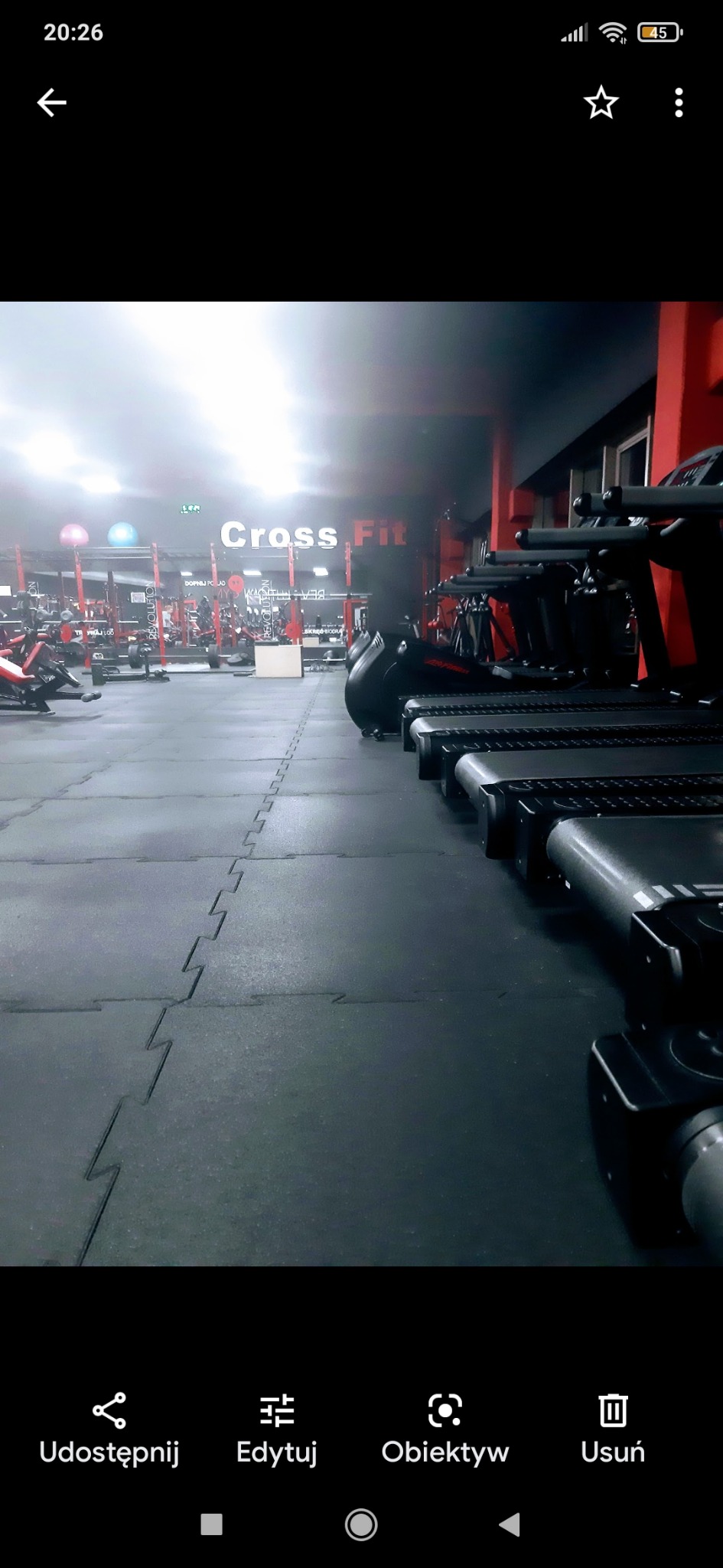 Wnętrze siłowni Cross Fit z rzędem bieżni, widoczne inne urządzenia do ćwiczeń w tle.