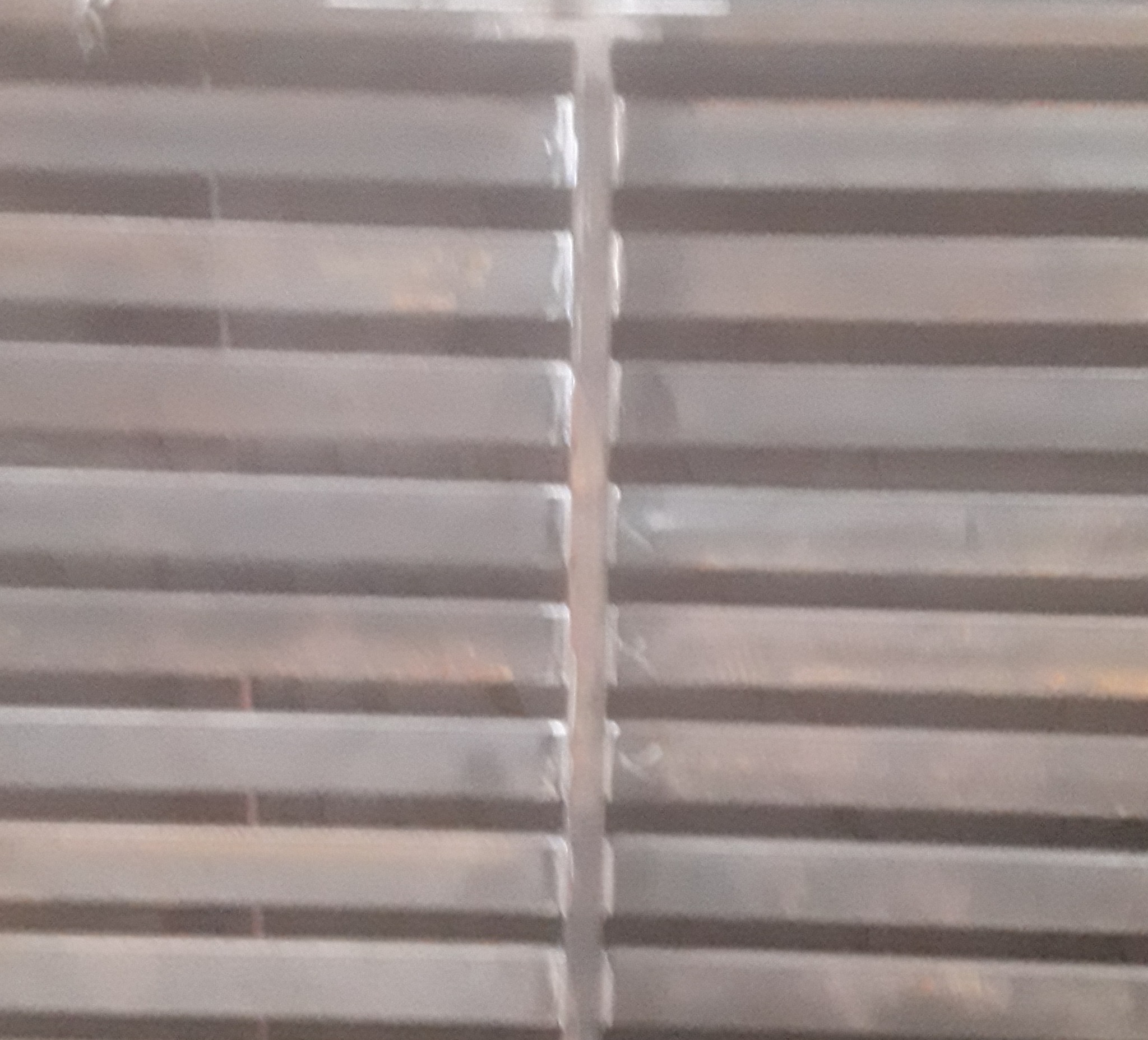 Szczegółowe zbliżenie spawanych, poziomych profili metalowych, tworzących konstrukcję bramy lub ogrodzenia, z widocznymi śladami spawania.