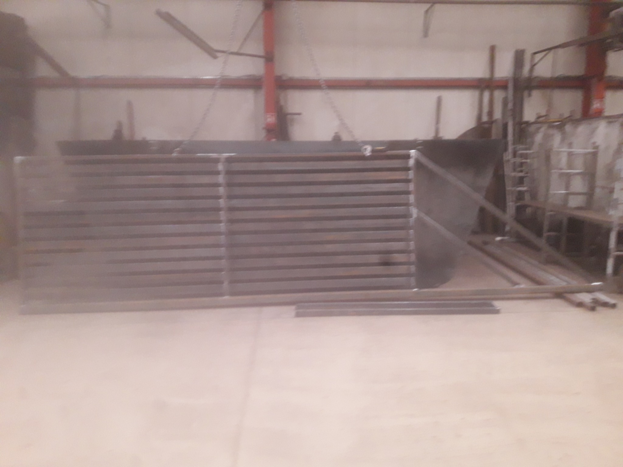 Metalowa konstrukcja bramy w trakcie produkcji, widoczne profile i elementy spawane, surowe wykończenie w hali produkcyjnej.