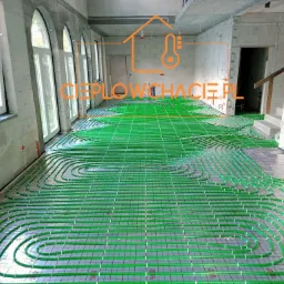 Zielone rury ogrzewania podłogowego ułożone na folii z siatką w surowym wnętrzu z oknami łukowymi i ścianami z betonu komórkowego przed wylewką.