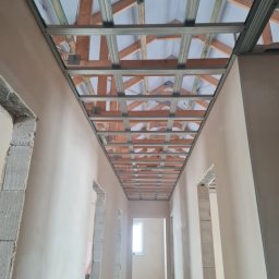 Usługi ogólnobudowlane - Wnętrze w trakcie wykańczania: widok na sufit z drewnianą konstrukcją i metalowymi profilami, ściany pokryte gładzią, otwory drzwiowe w trakcie obróbki.