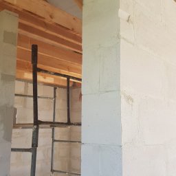 Usługi ogólnobudowlane - Wnętrze w trakcie budowy: ściany z białych bloczków, widoczne drewniane krokwie dachu i metalowe rusztowanie.