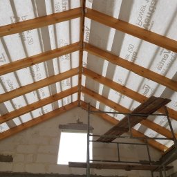 Usługi ogólnobudowlane - Konstrukcja dachu z drewnianych belek i membrany dachowej, widok z wnętrza budynku w trakcie budowy, z widocznym rusztowaniem i oknem.