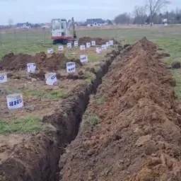 Wykop pod fundamenty z wyznaczonym obrysem, widoczny sprzęt budowlany i oznaczone punkty, teren budowy na zewnątrz.
