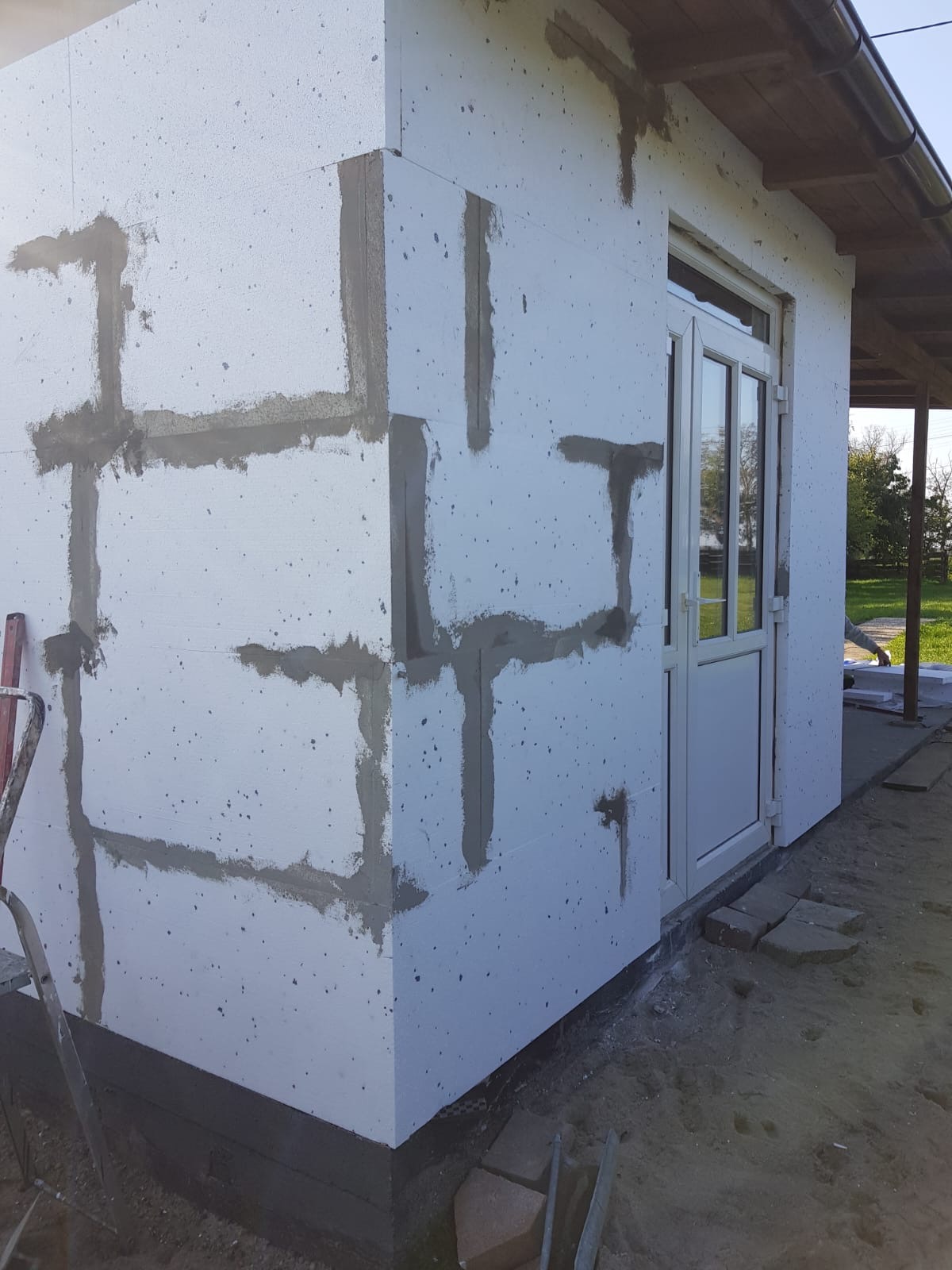 Ocieplanie elewacji budynku styropianem z widocznymi paskami kleju mocującego, przygotowanie do nałożenia siatki i tynku.