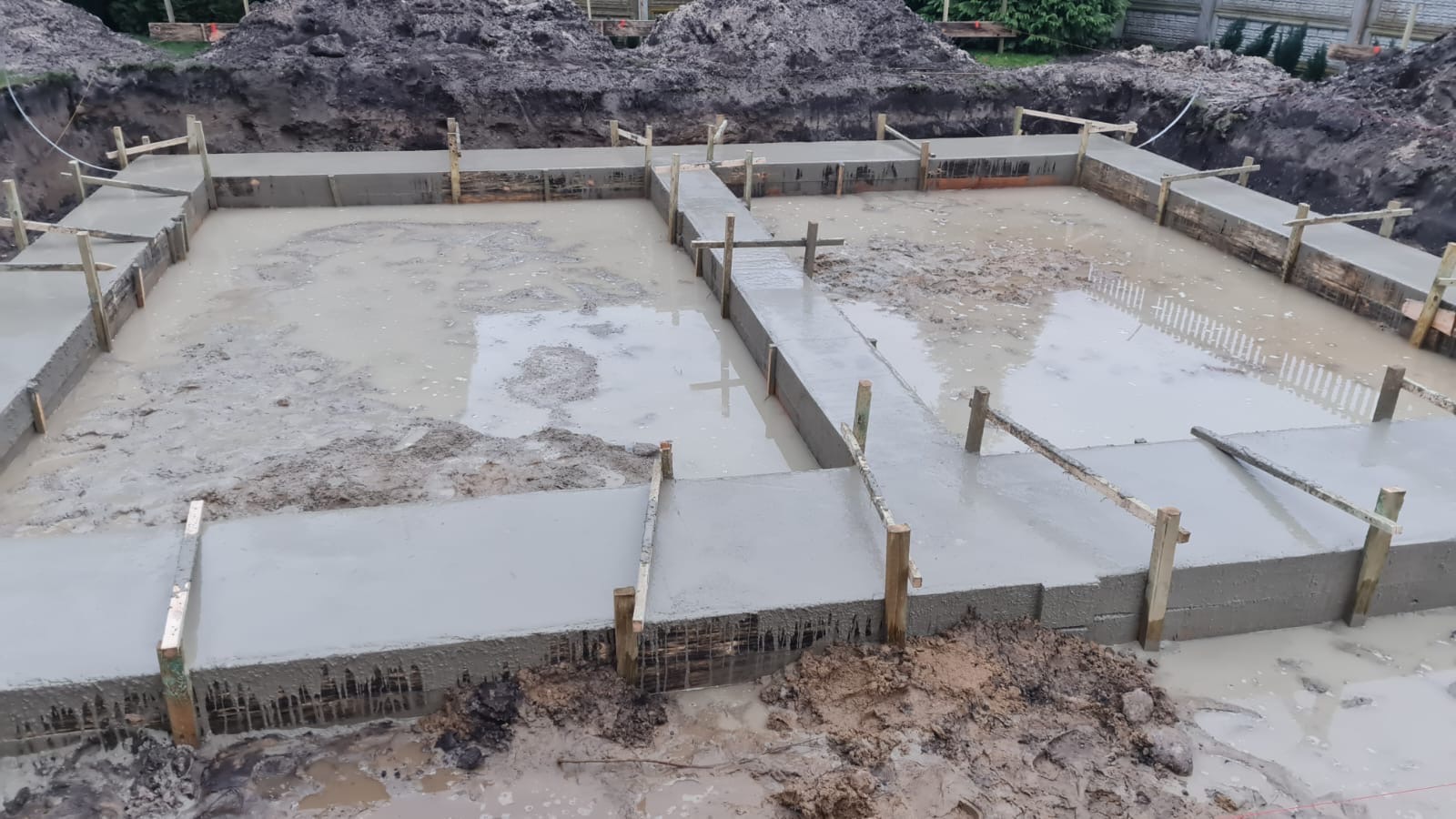 Zalany betonem fundament z drewnianym szalunkiem w wykopie wypełnionym wodą.