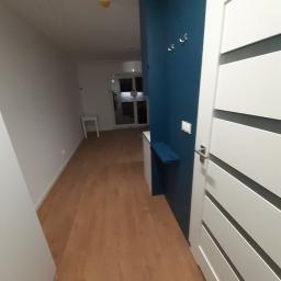 Usługi remontowe K.Kawecki firma: Reivilo - Nowoczesny przedpokój z drewnianą podłogą, białą ścianą, niebieską ścianą z wieszakami i półką, oraz białą, panelową drzwią.