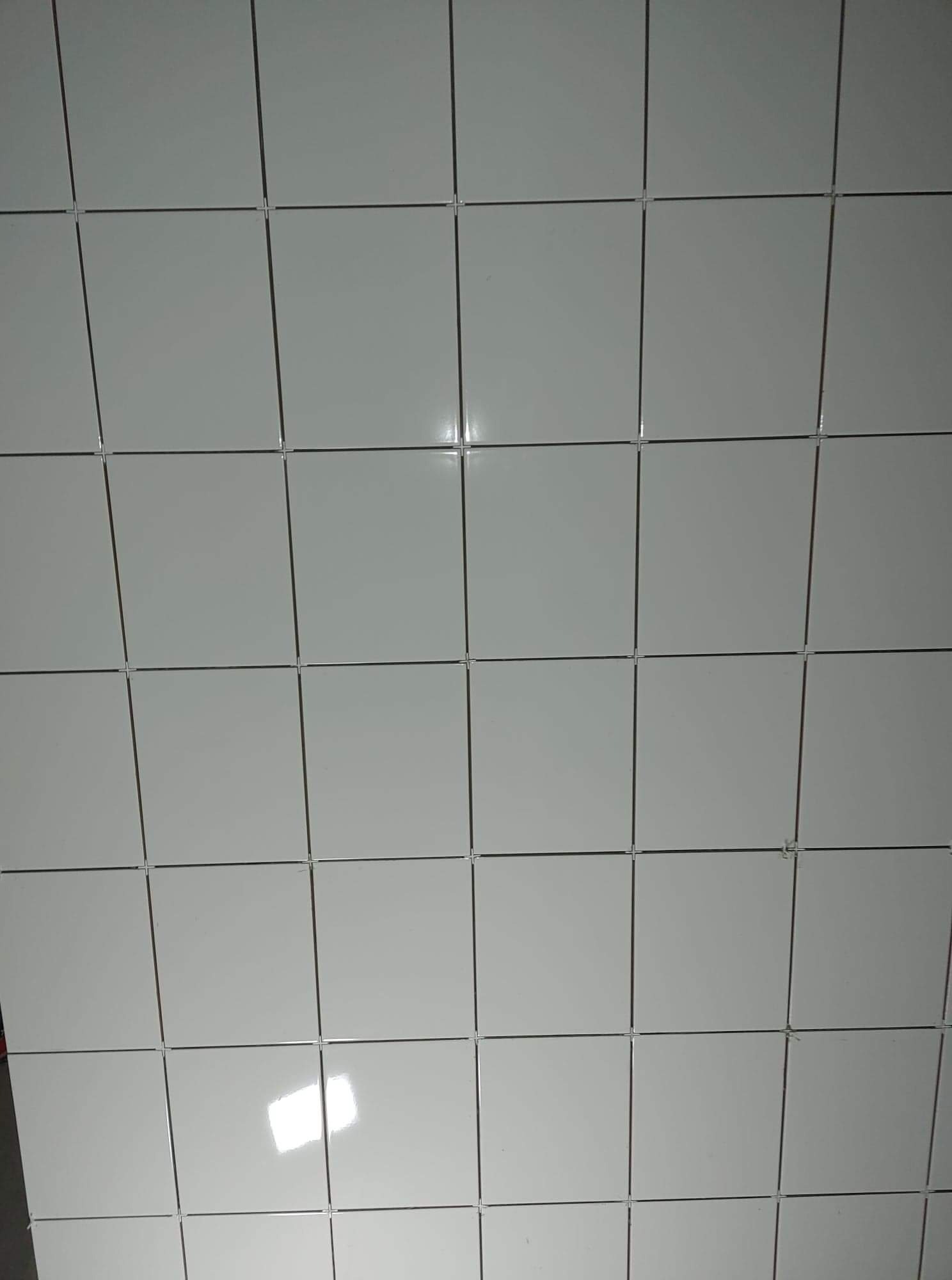 Świeżo położone, błyszczące, białe płytki ścienne z krzyżykami dystansowymi w spoinach, widoczne odbicie światła.