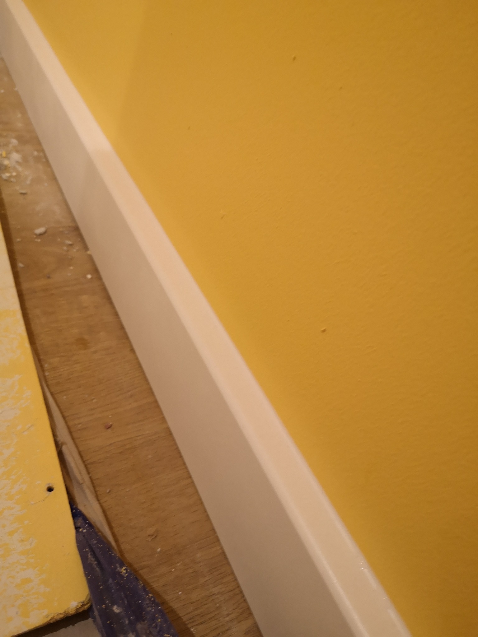 Żółta ściana z białą listwą przypodłogową w trakcie montażu w Poznaniu, widoczne drobne zabrudzenia i narzędzia.