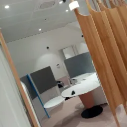 Nowoczesne biuro z białymi okrągłymi stolikami, szarymi panelami akustycznymi i drewnianą ścianką działową z pionowych listew.