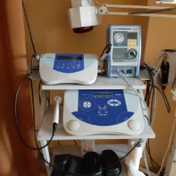 Wyposażenie gabinetu fizjoterapii: aparat do krioterapii Cryo-T, aparat do elektroterapii oraz lampa do światłolecznictwa na białym regale.