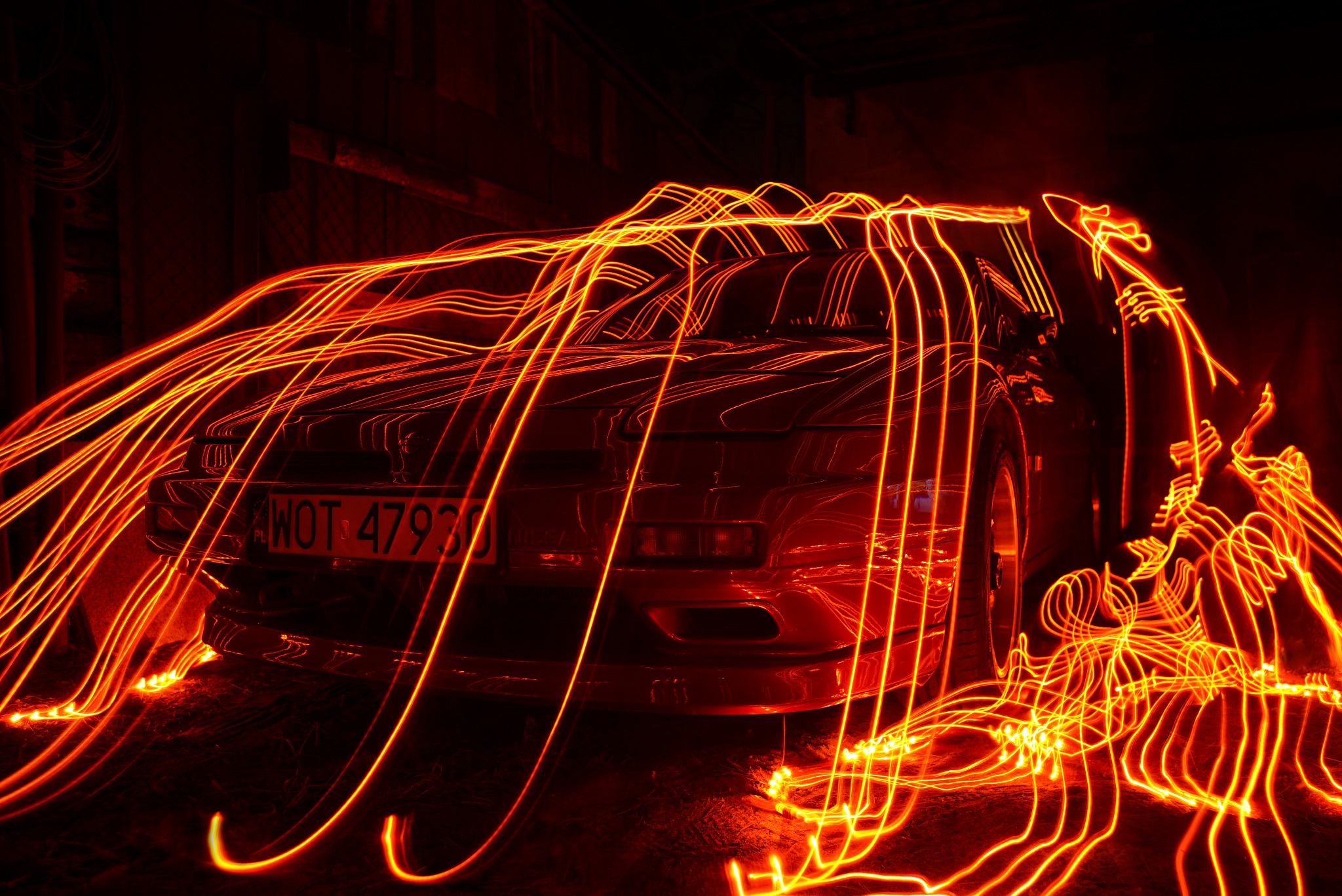 Czerwony sportowy samochód sfotografowany techniką light painting, tworzącą wokół niego abstrakcyjne, świetliste wzory.