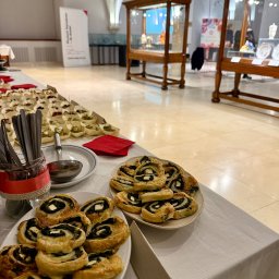 MadMad Maria Szafarkiewicz - Bufet z roladkami szpinakowymi z serem feta, mini kanapeczkami i sztućcami w słoiku na tle sali wystawowej z gablotami.