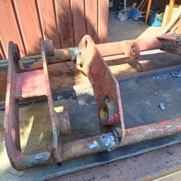 WELDEC Mobilne usługi spawalniczo-ślusarskie - Częściowo odnowiona, spawana konstrukcja metalowa pomalowana na czerwono, z widocznymi śladami spawania, leżąca na drewnianym podłożu, w warsztatowym otoczeniu.