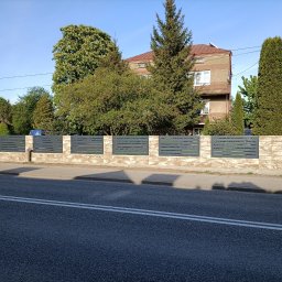 WELDEC Mobilne usługi spawalniczo-ślusarskie - Nowoczesne, poziome, szare przęsła ogrodzeniowe zamontowane na niskim murku z beżowych płytek, na tle dwupiętrowego budynku w otoczeniu zieleni.