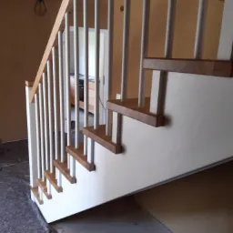 Nowoczesne schody z drewnianymi stopniami i białymi balustradami, widoczne zabezpieczenia podłogi podczas montażu.