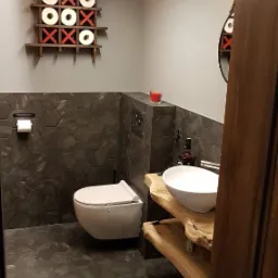 Nowoczesna łazienka z heksagonalnymi płytkami w odcieniach szarości, podwieszana toaleta, umywalka nablatowa na drewnianym blacie z surowego drewna, dekoracja ścienna z papieru toaletowego...