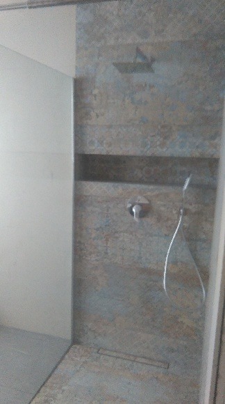 Nowoczesna kabina prysznicowa walk-in z szarą mozaiką na ścianie, deszczownicą i odpływem liniowym w podłodze.