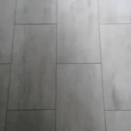 Ułożone szare panele podłogowe o wzorze drewna, z widocznymi fugami, ułożone w nieregularny wzór.