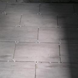 Rem-bud - Ułożone płytki podłogowe w trakcie prac, z użyciem krzyżyków dystansowych, widoczne fragmenty niezakończonej powierzchni.
