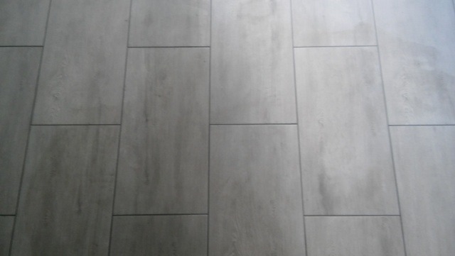 Ułożone szare panele podłogowe o wzorze drewna, z widocznymi fugami, ułożone w nieregularny wzór.