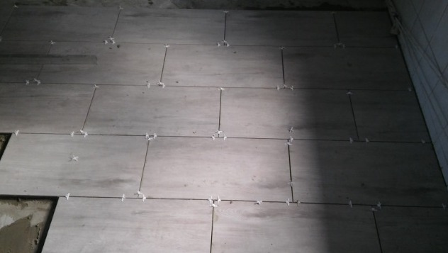 Ułożone płytki podłogowe w trakcie prac, z użyciem krzyżyków dystansowych, widoczne fragmenty niezakończonej powierzchni.